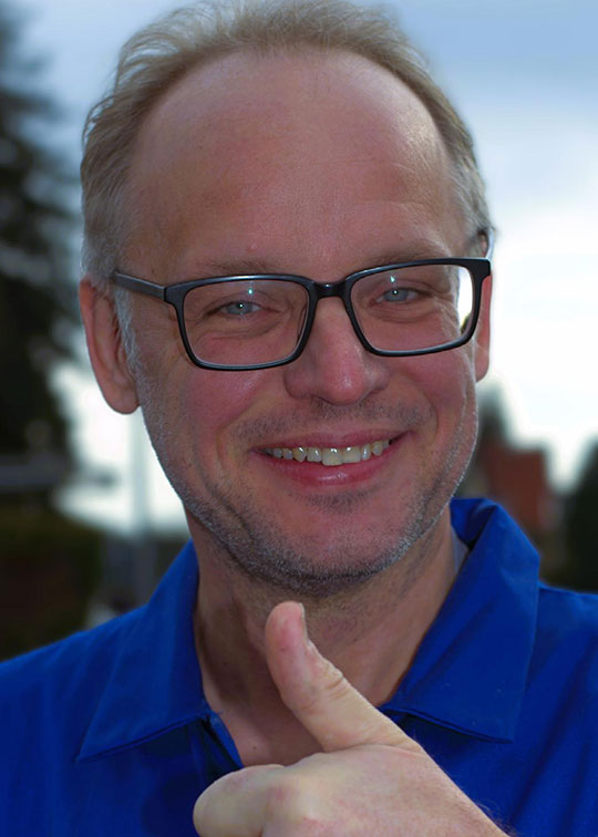 Jochen im blauen Arbeitsblaumann lächelnd mit Brille