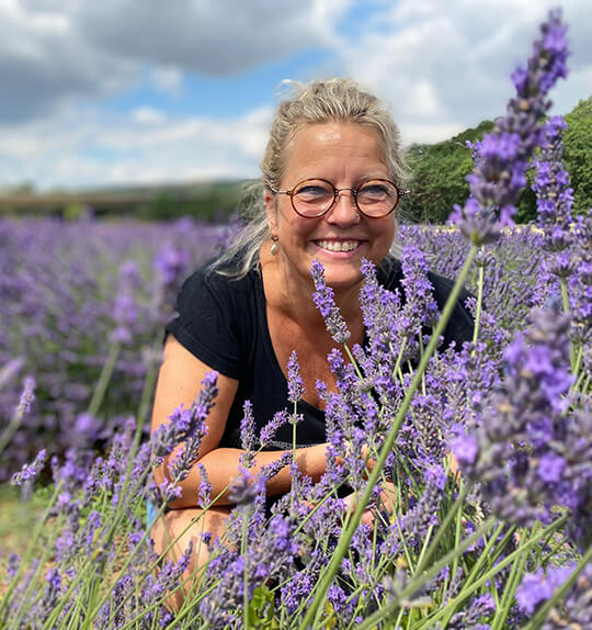 Caro mit Brille in Lavendelfeld, lächelnd mit Blüten