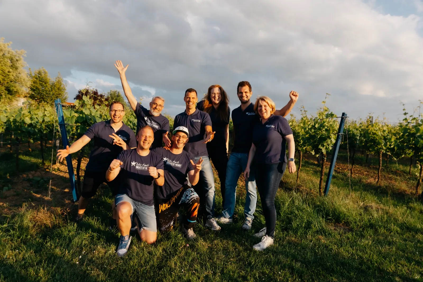 Sales-Angels-Team jubelnd im Weinberg mit erhobenen Armen