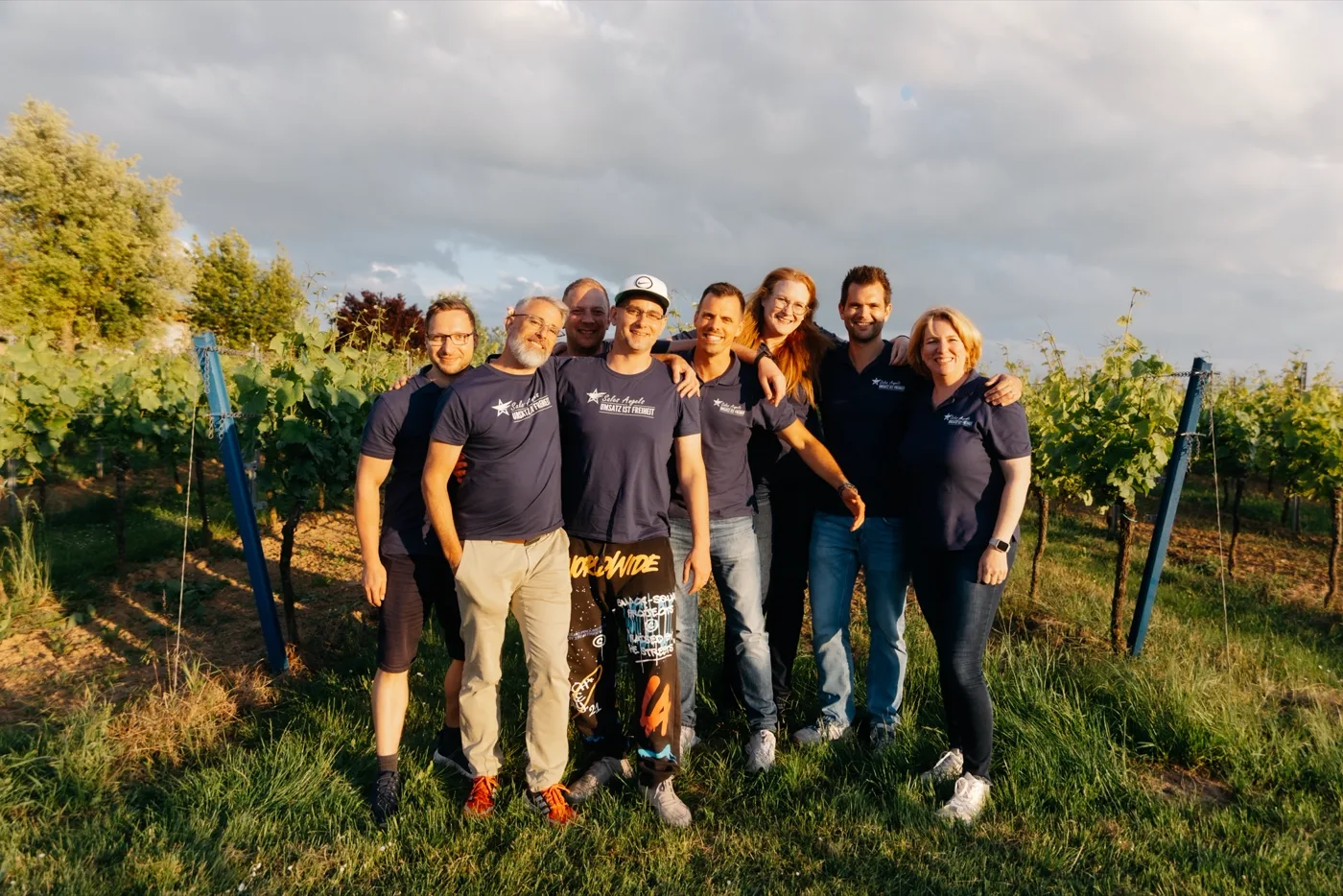 Sales-Angels-Team in entspannter Pose im Weinberg bei Sonnenuntergang