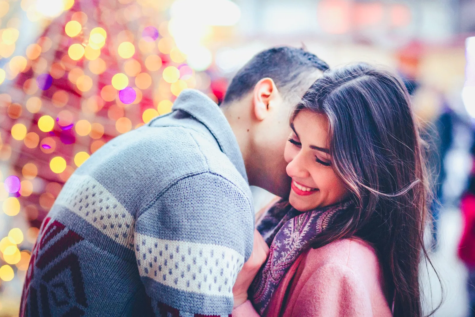 Junges Paar umarmt sich vor weihnachtlichem Bokeh-Hintergrund