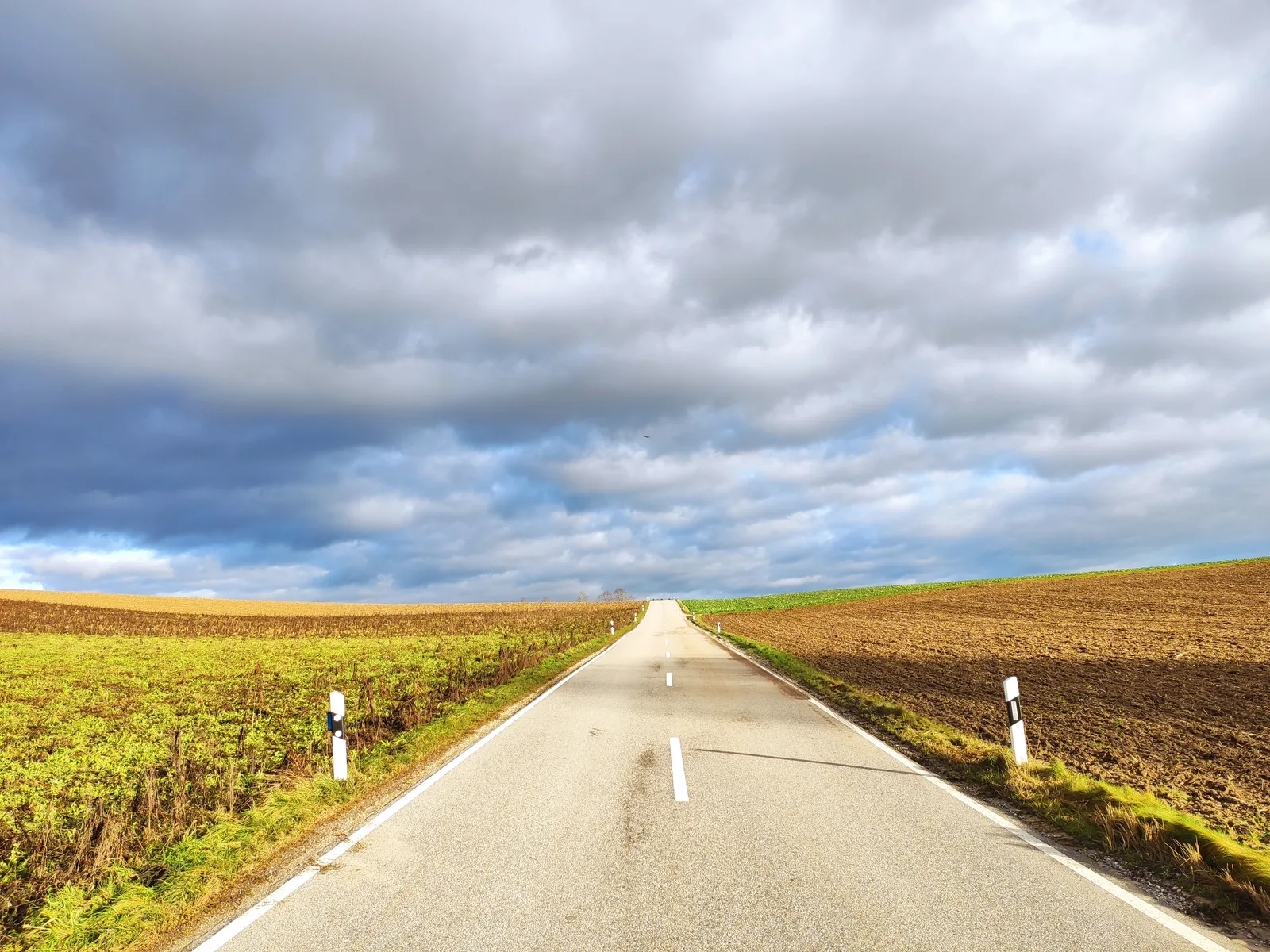 Lange gerade Straße durch Ackerland mit Feldern und dramatischem Himmel mit Wolken