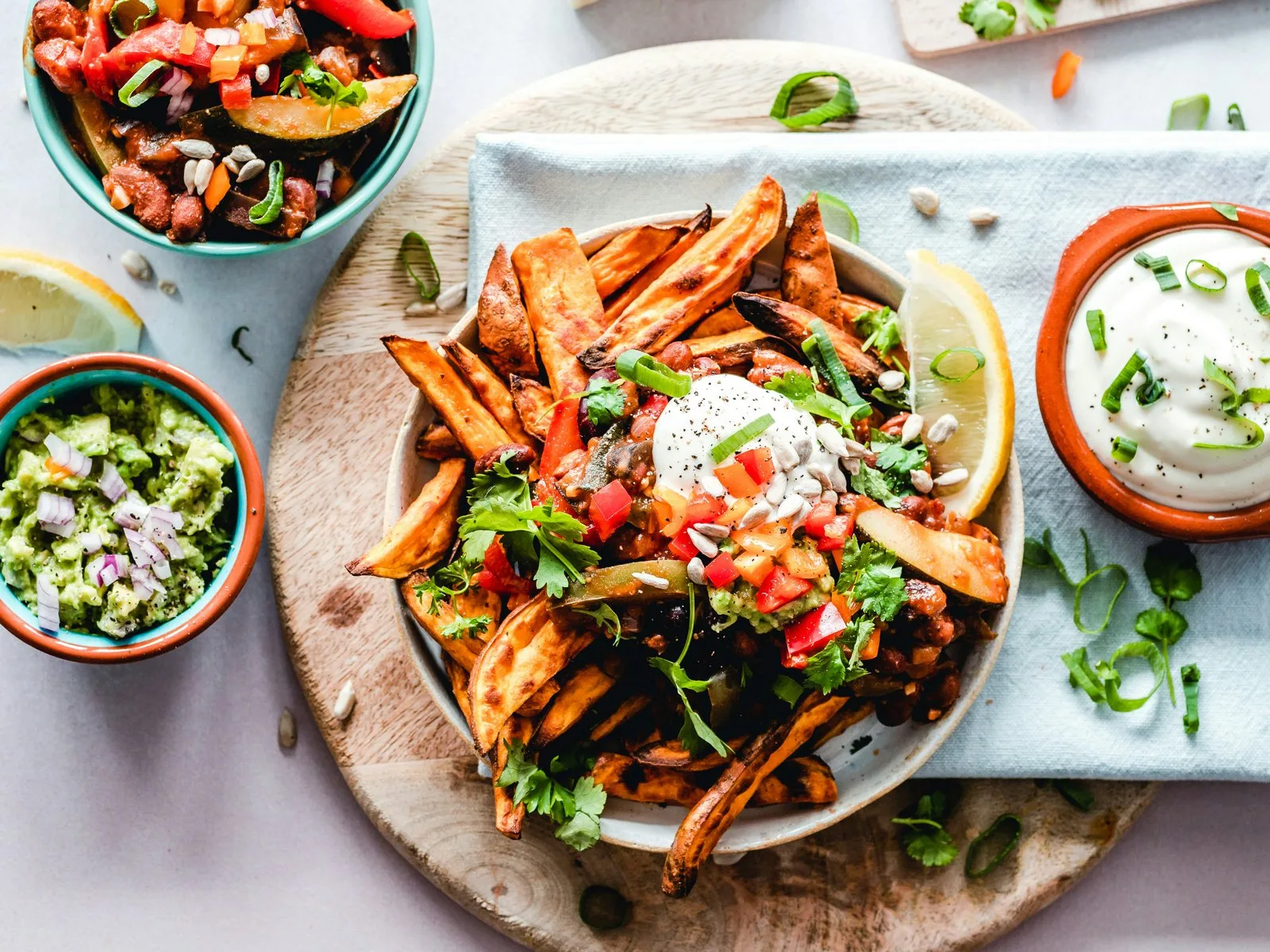 Teller mit Süßkartoffelspalten, weißem Dip, Guacamole und Salsa auf Holzbrett