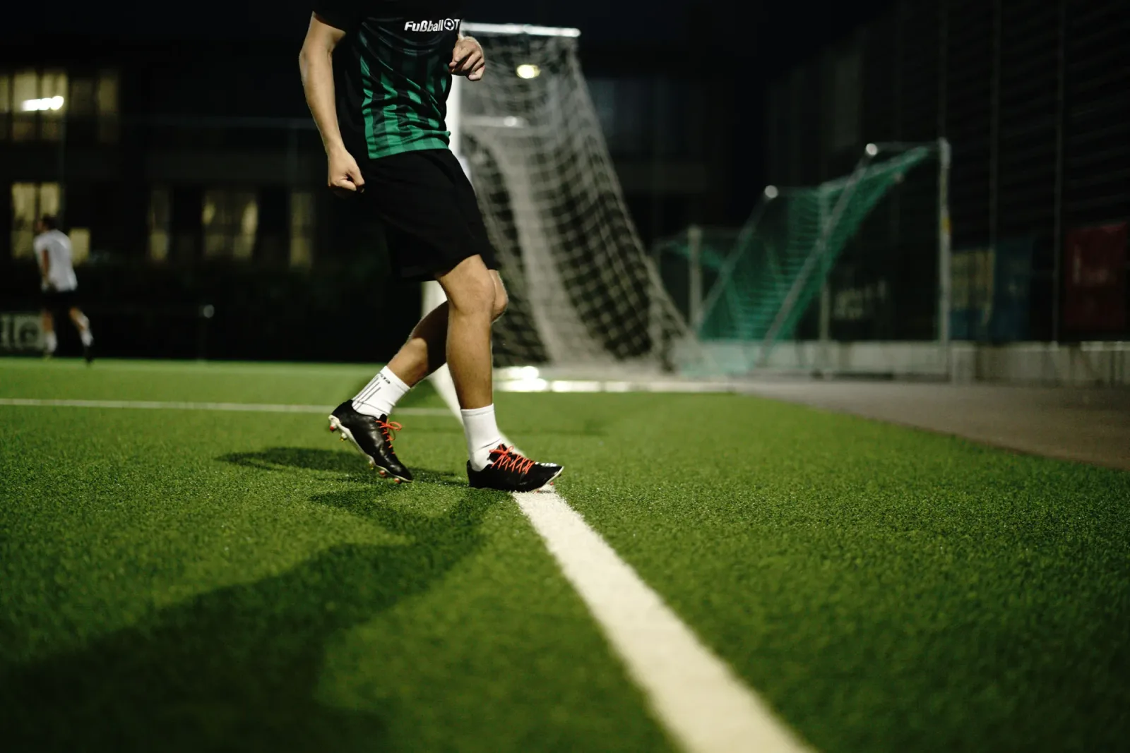 Fußballspieler dribbelt nachts auf beleuchtetem Platz vor Tor