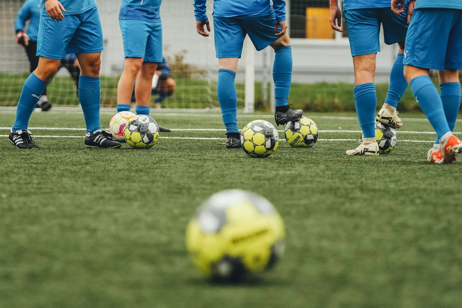 Fußballmannschaft in blauen Trikots und Stutzen steht im Kreis um mehrere Fußbälle auf Kunstrasenplatz