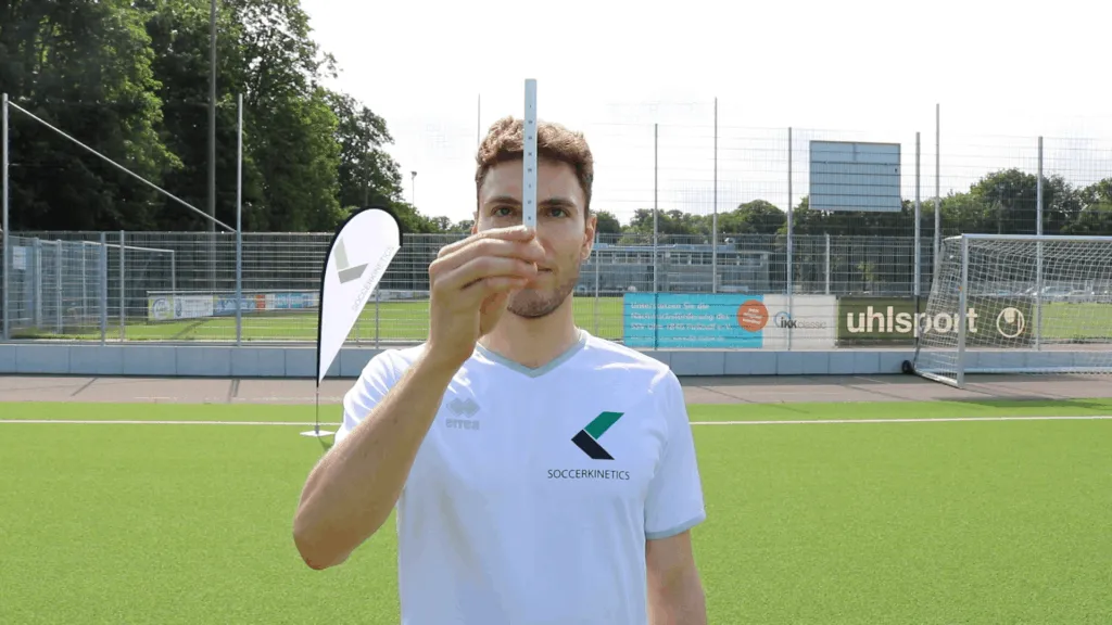 Spieler in weißem Soccerkinetics-Shirt hält blaues visuelles Trainingstool auf Fußballplatz