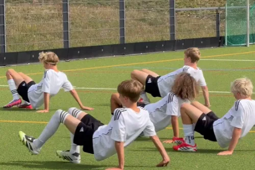 Kinder in Trainingskleidung führen Animal Moves Übungen (Krabbengang, Bärenstütz) auf Rasenplatz durch