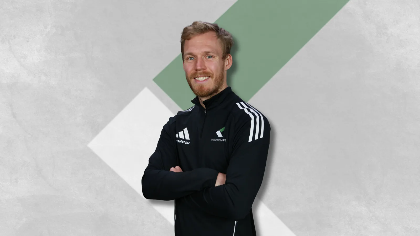 Porträt Fußballtrainer Philipp Ludwig in schwarzem Adidas-Trainingsjacke mit verschränkten Armen vor geometrischem Hintergrun
