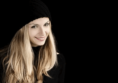 Junge Frau mit schwarzem Beanie und hellblonden Haaren vor schwarzem Hintergrund