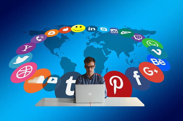 Man mit Laptop umgeben von Social-Media-Plattform-Icons auf Weltkarte