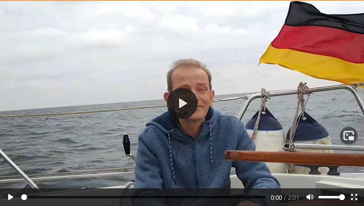Videostandbild: Mann auf Segelboot mit deutscher Flagge, Play-Symbol sichtbar