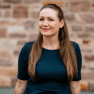 Porträtfoto einer Frau mit braunem Haar vor Backsteinwand