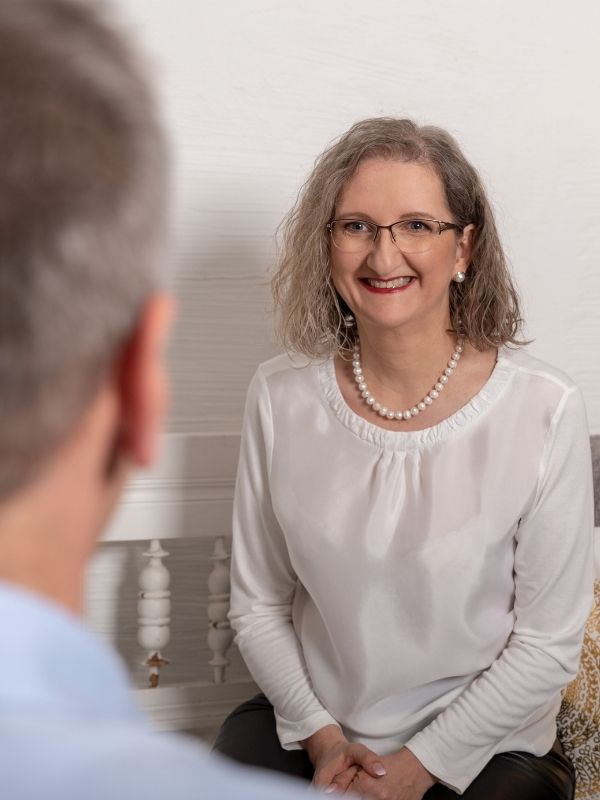 Gabriele Strasky in weißer Bluse mit Perlenkette während eines Erstgespräches, lächelnd