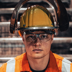 Portrait: Mann in Arbeitsschutzausrüstung mit Helm und Schutzbrille in orange-gelb