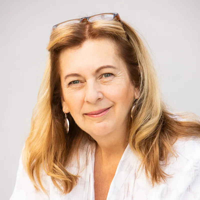 Porträt von Angelika E. Hohenberger mit Sonnenbrille, weißes Hemd vor grauem Hintergrund