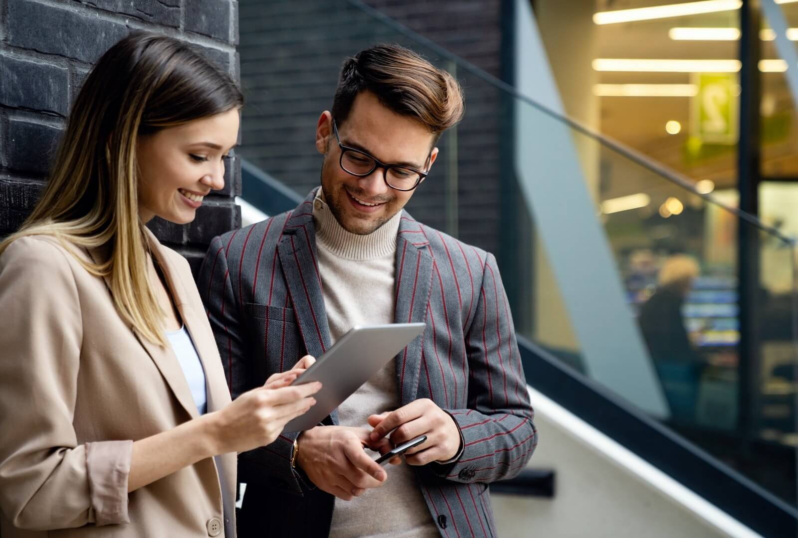 Zwei Geschäftsleute mit Tablet vor dunkler Fassade, modernes Business Setting
