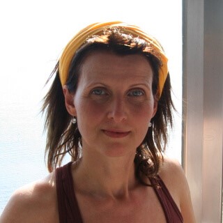 Frau mit braunem Haar am Fenster, neutraler Gesichtsausdruck