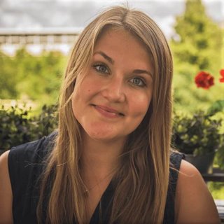 Blonde Frau lächelt in die Kamera vor grünem Gartenhintergrund