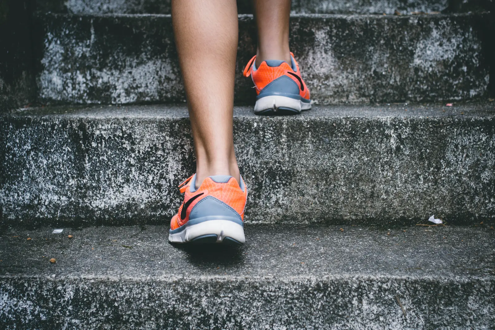 Nahaufnahme von Beinen in orangenen und grauen Laufschuhen auf Betonstufen