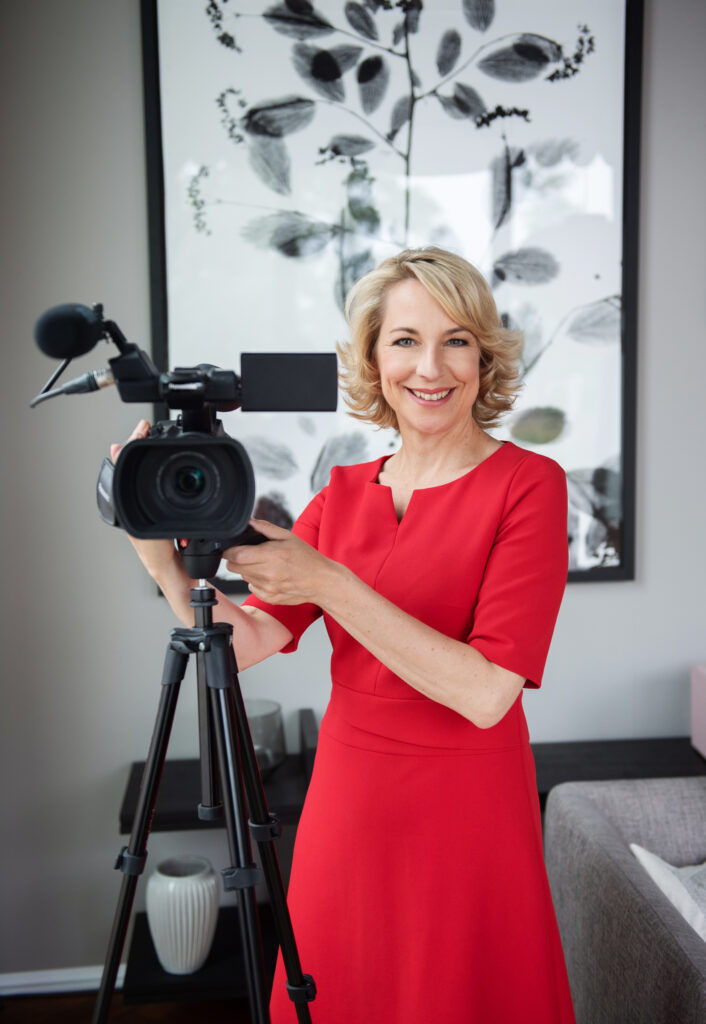 Frau in rotem Kleid mit Videokamera auf Stativ vor Kunstwerk
