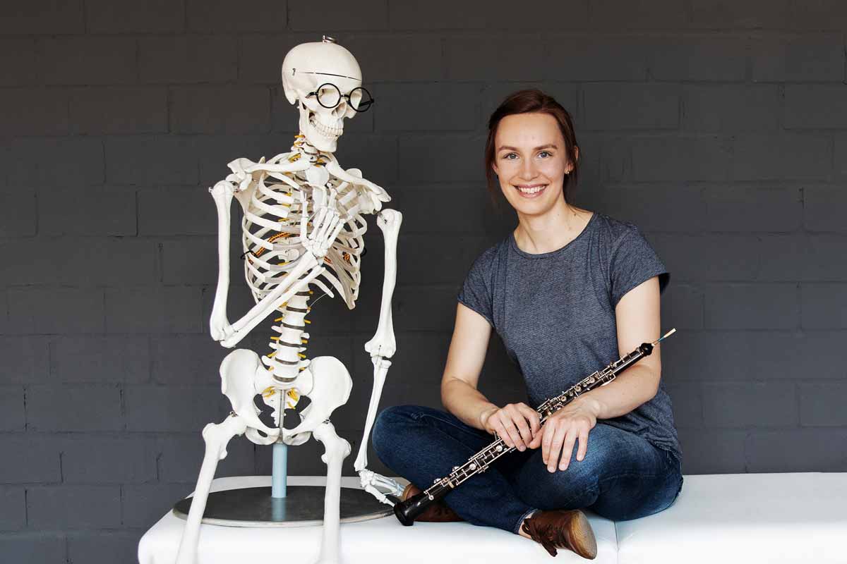 Sophie Stahl mit Oboe neben anatomischem Skelett-Modell, Porträtfoto für Webinar
