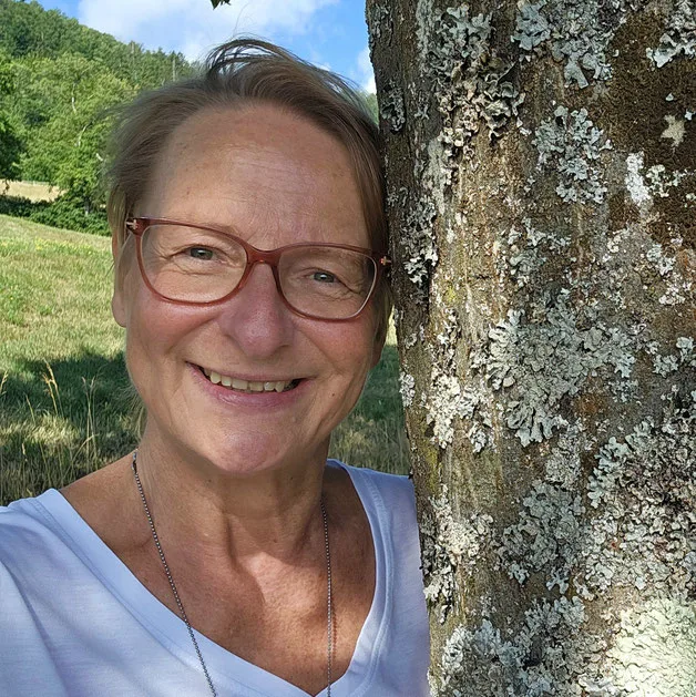 Quadratisches Porträtfoto von Dr. Kerstin Joost mit Brille, lächelnd vor Baumrinde