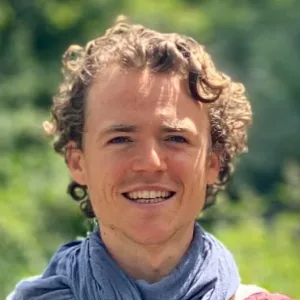 Porträtfoto von Philip Kunisch lächelnd mit lockigem Haar vor grünem Naturhintergrund