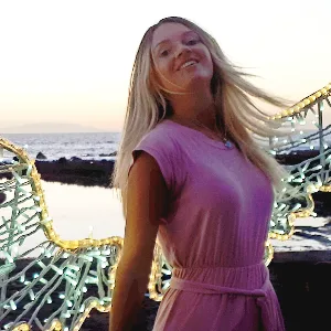 Porträtfoto von Sandrina in pinkem Kleid am Meer mit Sonnenuntergang im Hintergrund