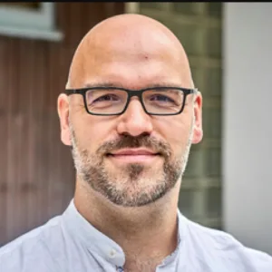 Porträt von Fabian Strumpf, Mann mit Brille und Bart im weißen Hemd
