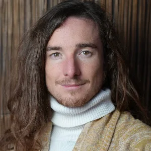Portrait Robin Kaiser – Mann mit langen dunklen Haaren und gelbem Pullover