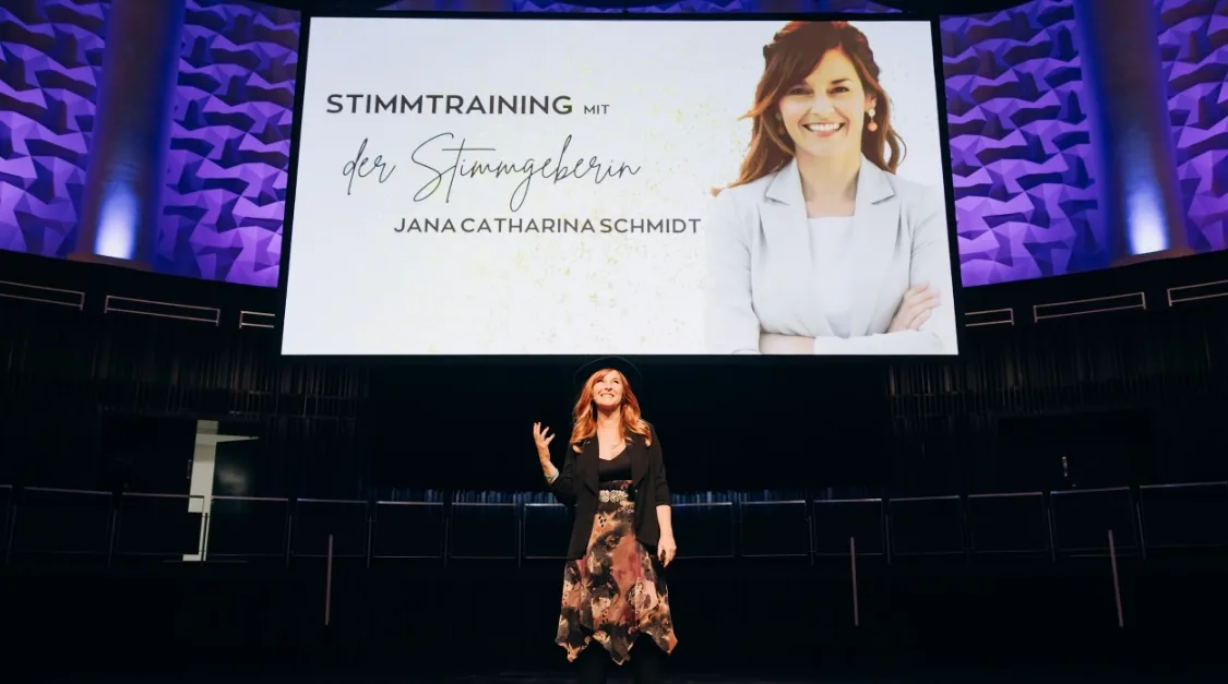 Jana Catharina Schmidt bei Bühnenauftritt mit Großbildschirm-Präsentation
