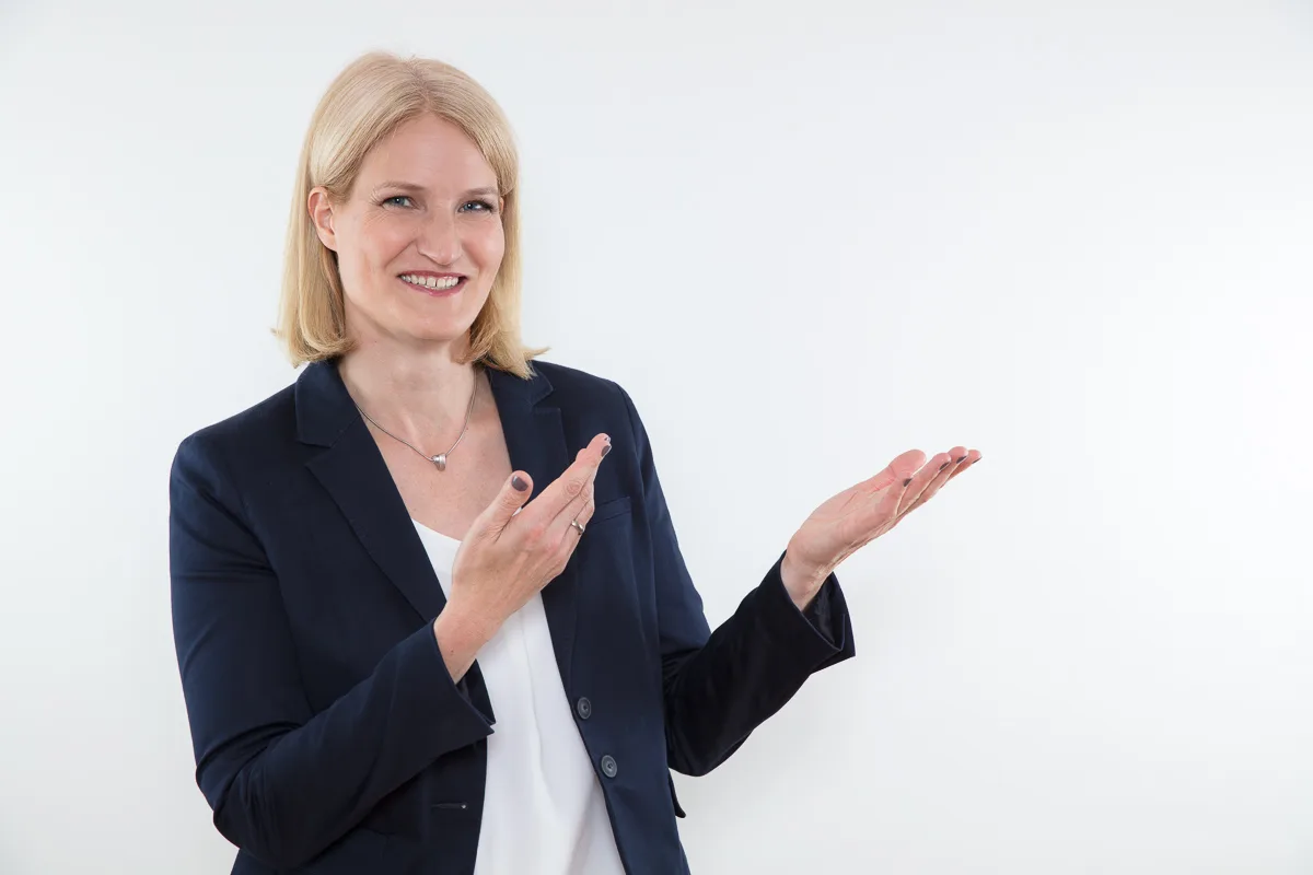 Story klar – Erzählcoaching für Experten von Insa Künkel 8 Insa Künkel, blonde Frau in dunklem Blazer mit weißer Bluse, Finger zeigend, Lächeln