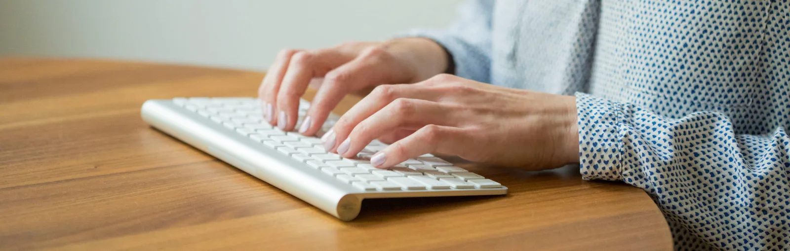 Story klar – Erzählcoaching für Experten von Insa Künkel 5 Hände tippen auf weißer Tastatur auf braunem Schreibtisch, blaues Muster-Oberteil