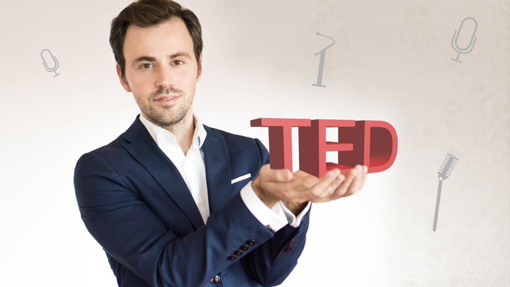 TED-Talk Online-Kurs Kover: Mann präsentiert TED-Schriftzug mit Mikrofonen