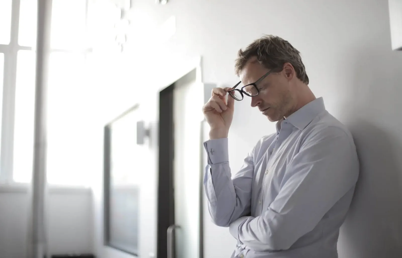 Mann mit Brille in hellem Büro, nachdenklich, hand an Brille, Fenster im Hintergrund