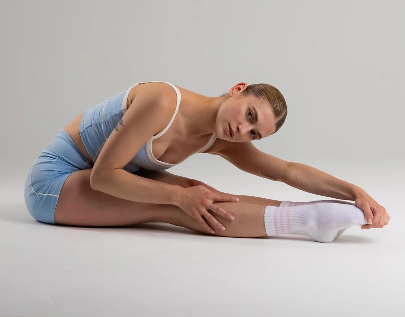 Frau in blauem Sportoutfit dehnt sitzend nach vorne, Hamstring-Stretch
