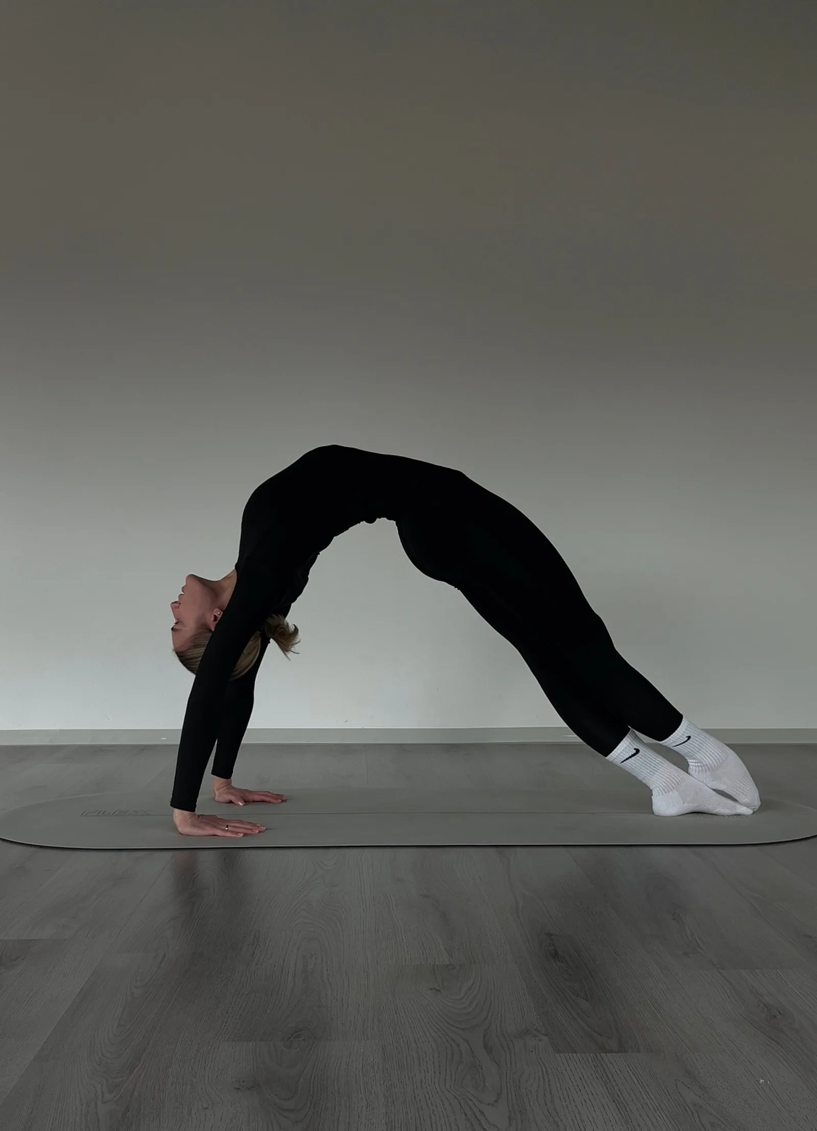 Frau in Brückenpositur auf Yogamatte, invertierte Rückbeuge, schwarze Sportkleidung