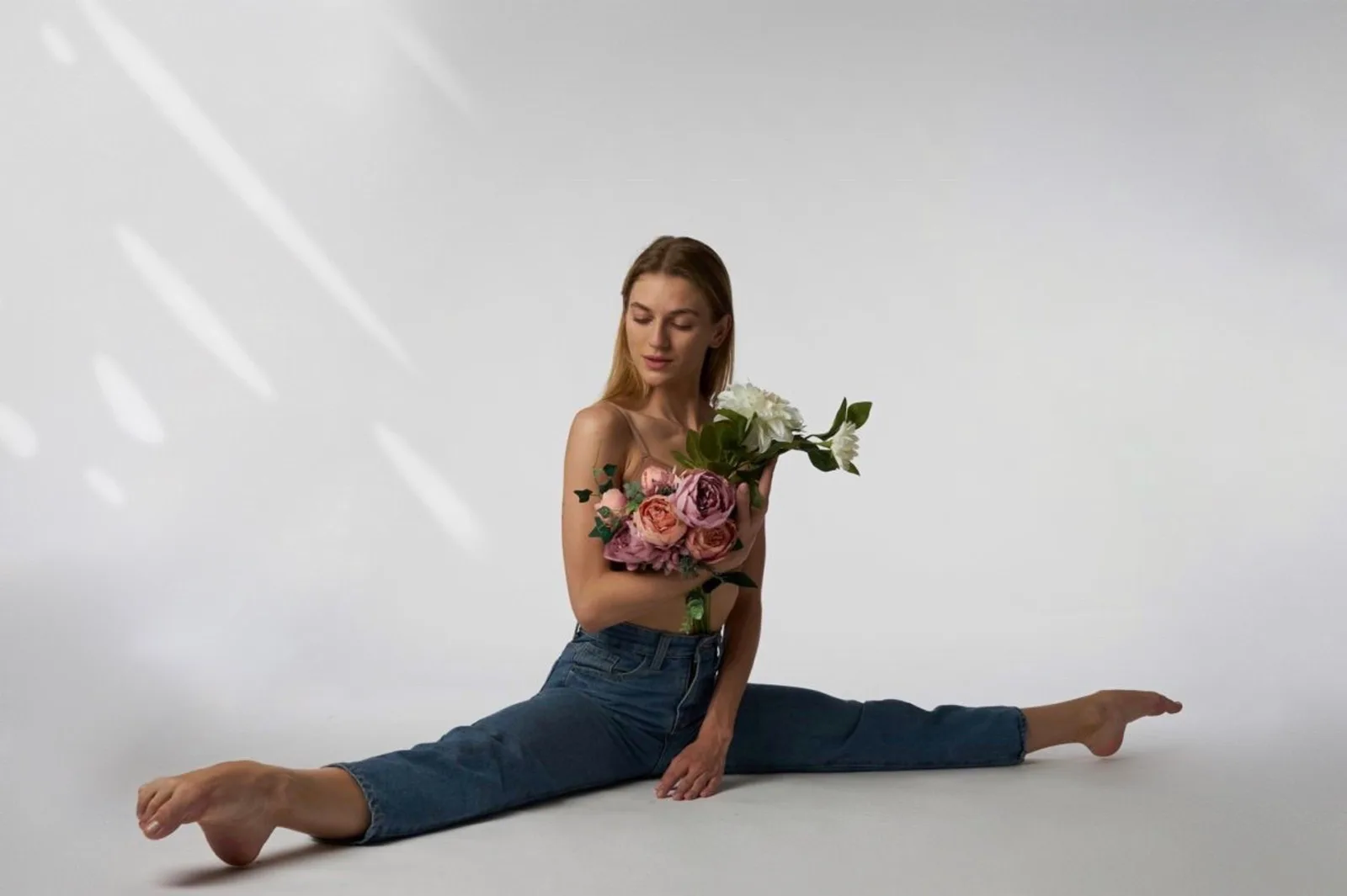 Frau in Spagat mit Blumenstrauß, Jeans und schwarzes Top, weißer Hintergrund