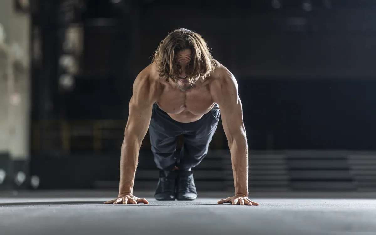Mann in Trainingsposition beim Push-up auf grauer Bodenfläche, Fitnesstraining