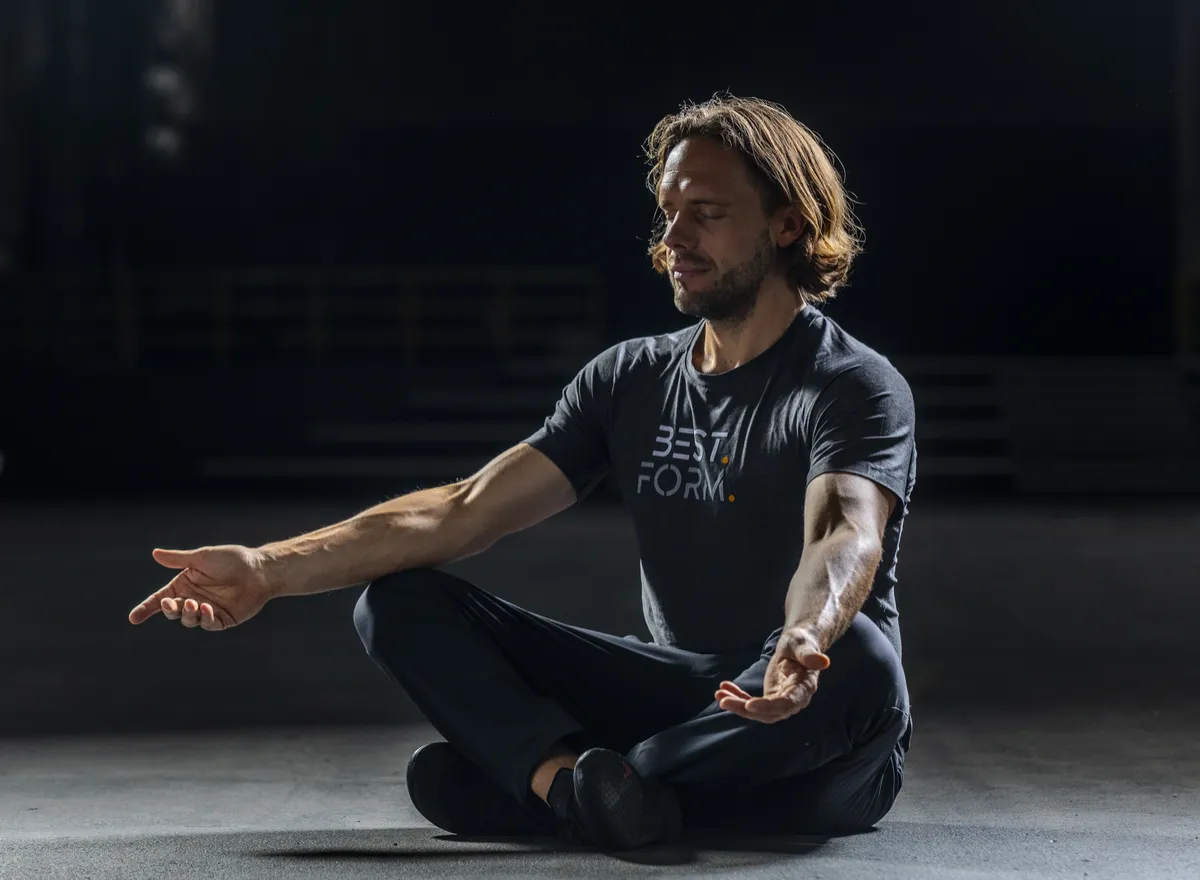Mann in Best Form T-Shirt sitzt in Meditationshaltung auf grauem Untergrund