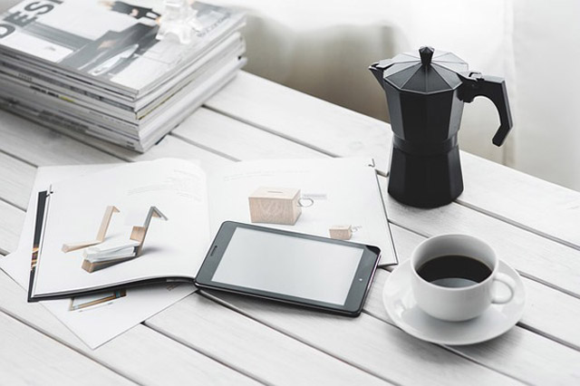 Arbeitsplatz mit Tablet, Notizbuch, Stift, italienischer Kaffeekanne und Kaffee auf weißem Schreibtisch
