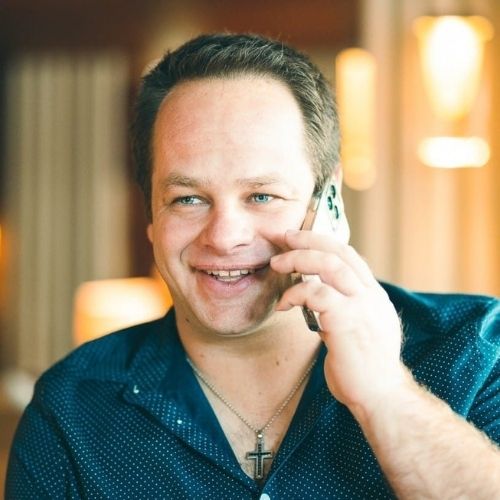 Porträtfoto von Mike Wilhelmer am Telefon mit dunklem Hemd und Kreuz-Kette