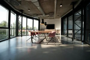 Modernes Büro mit Betondecke, großem Esstisch aus Holz, burgunderroten Stühlen und Panoramafenstern