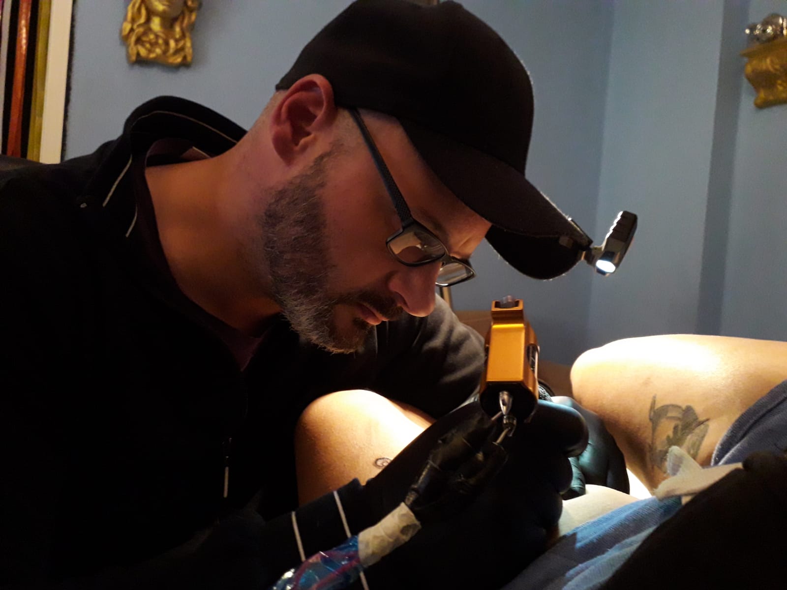 Tattoo-Künstler Luigi beim Tätowieren, konzentriert über Kundenarm gebeugt mit Tätowiermaschine