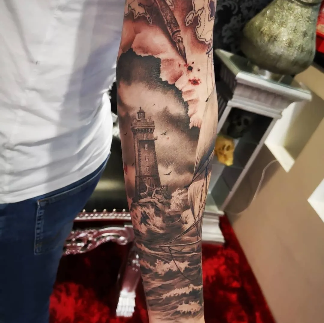 Landschafts-Tattoo am Arm: Leuchtturm mit Nebel und Wald-Szenerie in Farbe und Grautönen