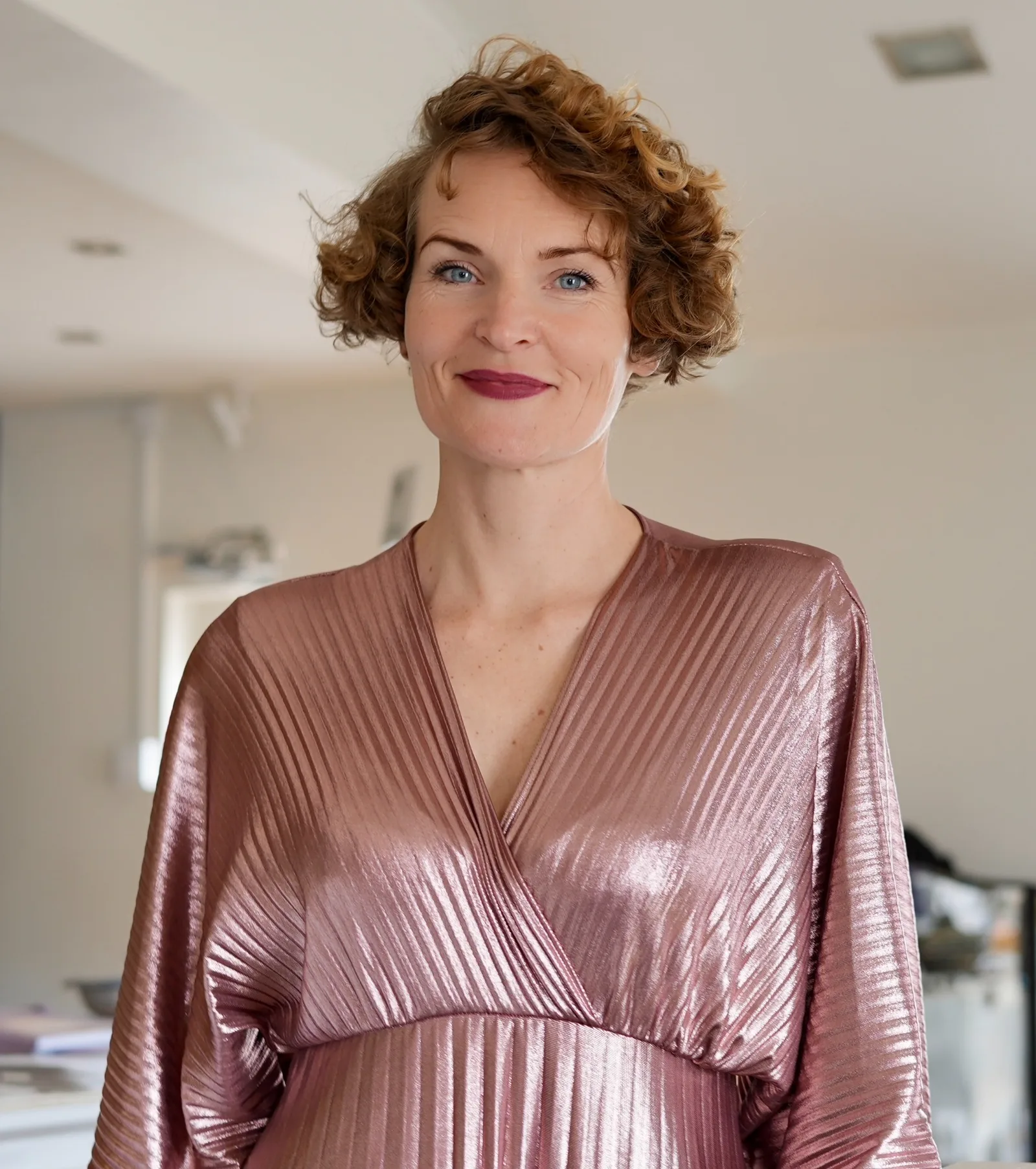 Stefanie Bruns, Frau mit kupferfarbenen Locken in altrosa glänzendem Wickelkleid, Porträt