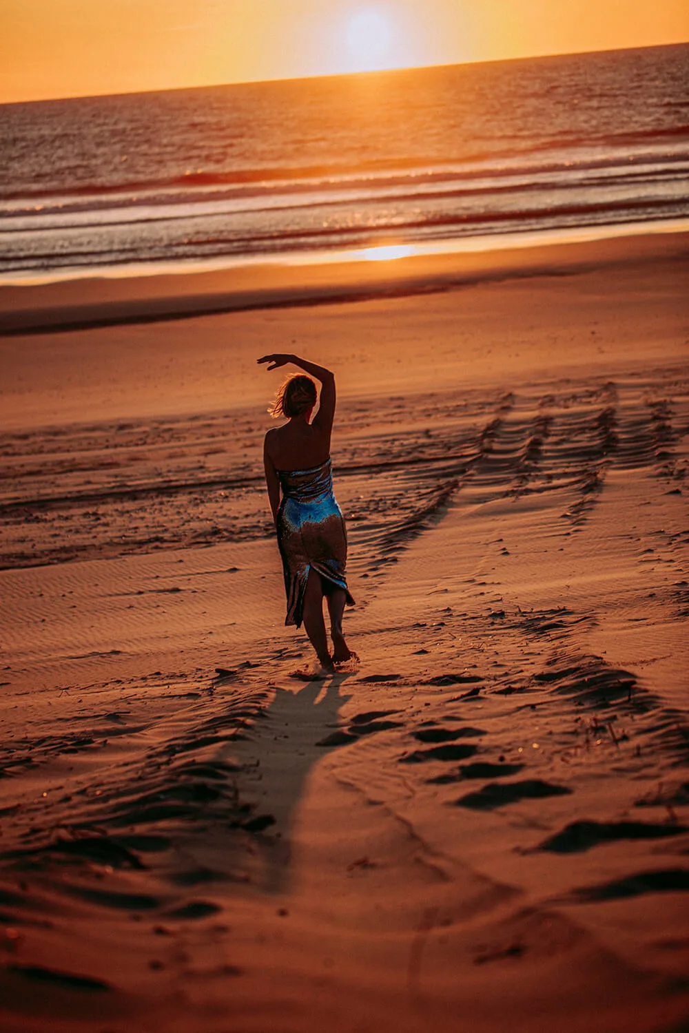 Frau bei Sonnenuntergang am Strand, seitliche Dehnposition mit erhobener Hand