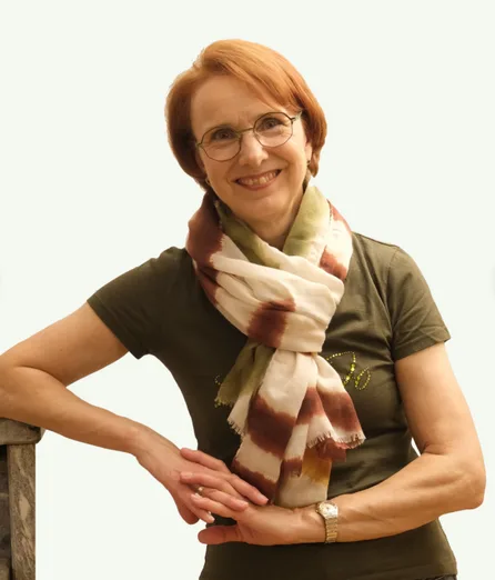 Gina Heller sitzt am Kamin, trägt olivgrünes Shirt mit Schal, lächelt in die Kamera