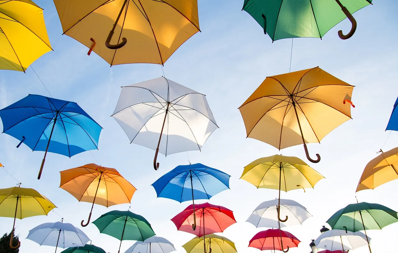 Bunte Regenschirme in Gelb, Orange, Blau und Rot hängend am Himmel, Vielfalt und Schutz