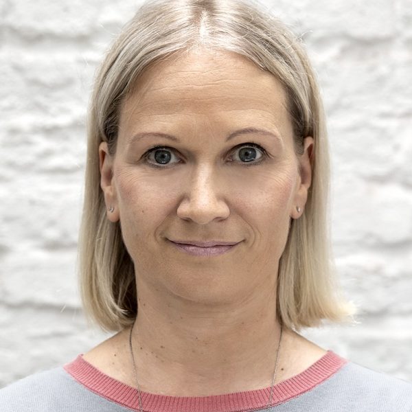 Porträt einer blonde Frau vor weißer Backsteinmauer in rosa Pullover